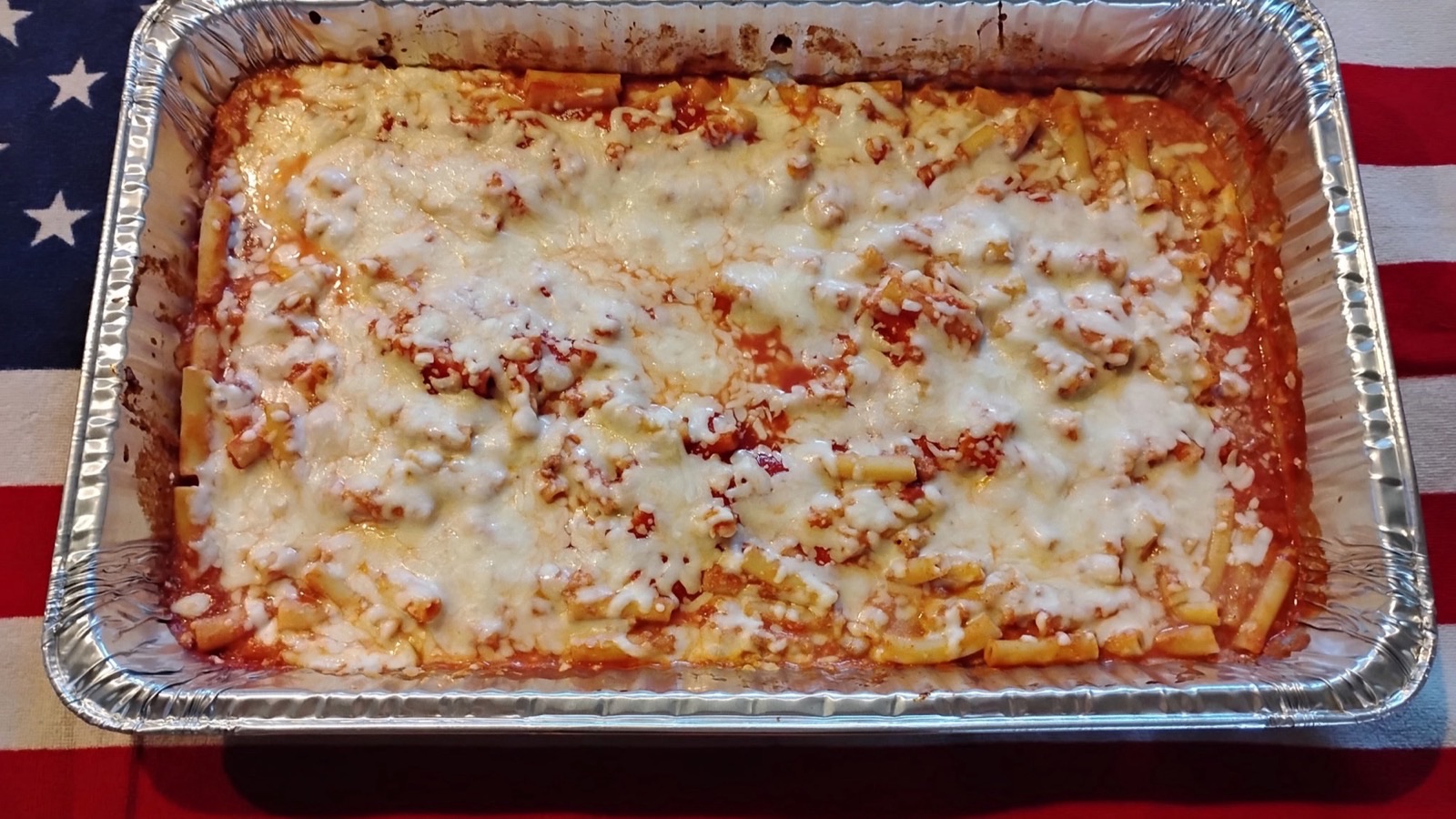 A catering pan of baked ziti in marinara topped with melted cheese
