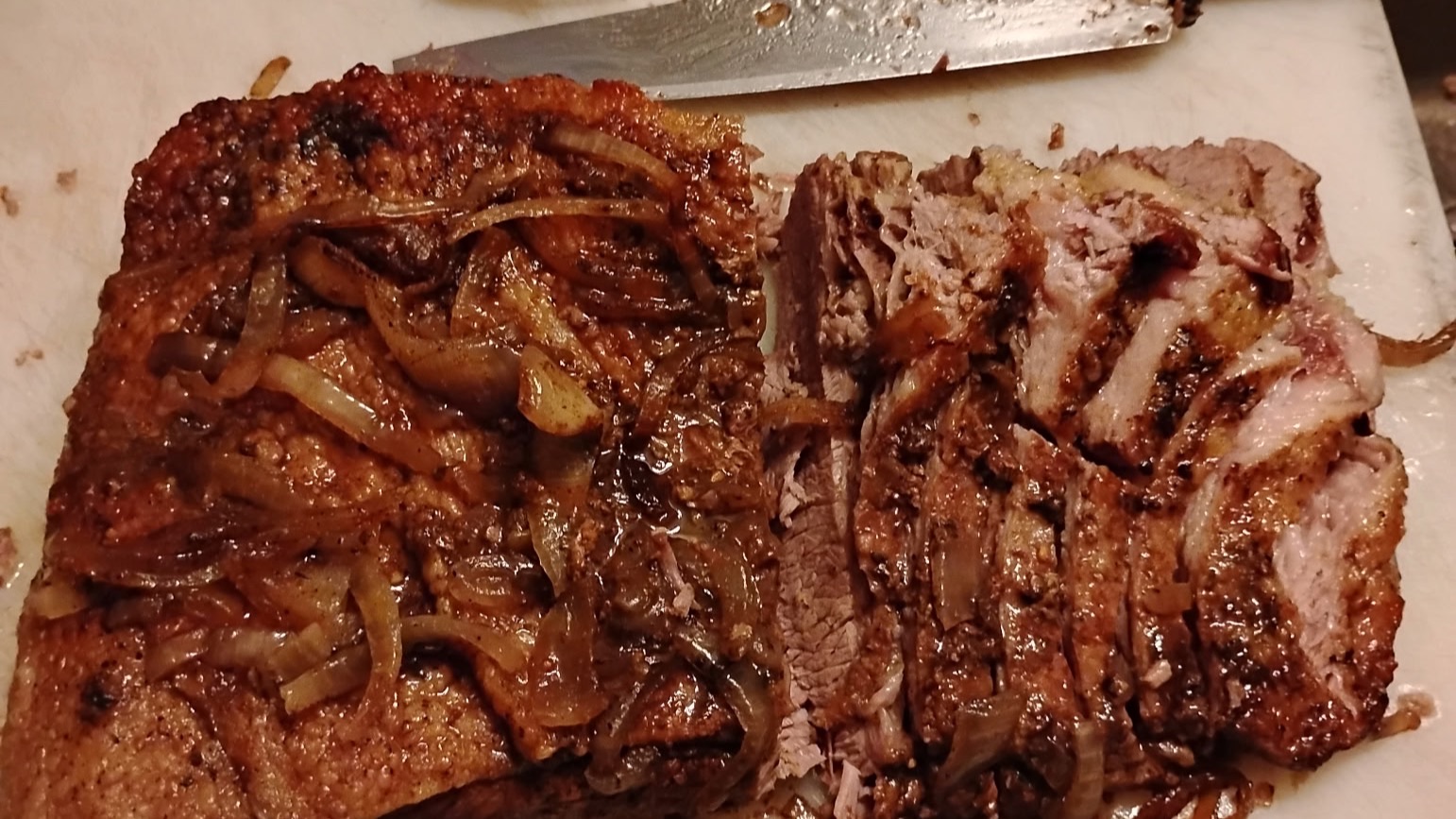 Slow baked beef brisket, hand sliced on a cutting board and topped with grilled onions