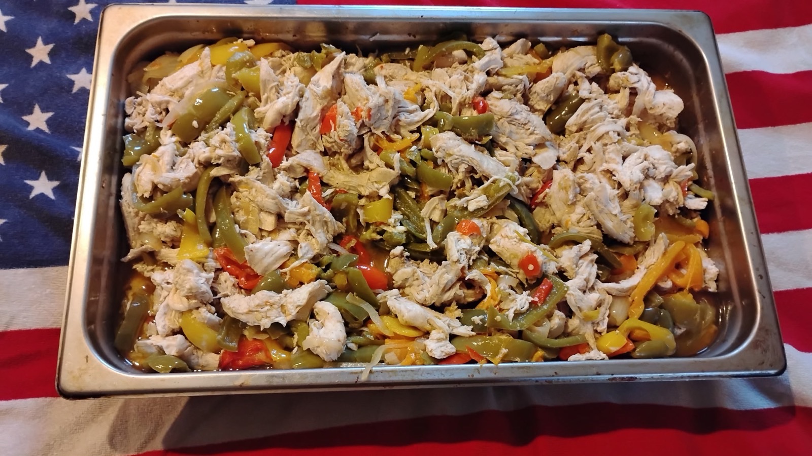 A catering tray of chicken fajitas with sliced red, green and yellow peppers and onions