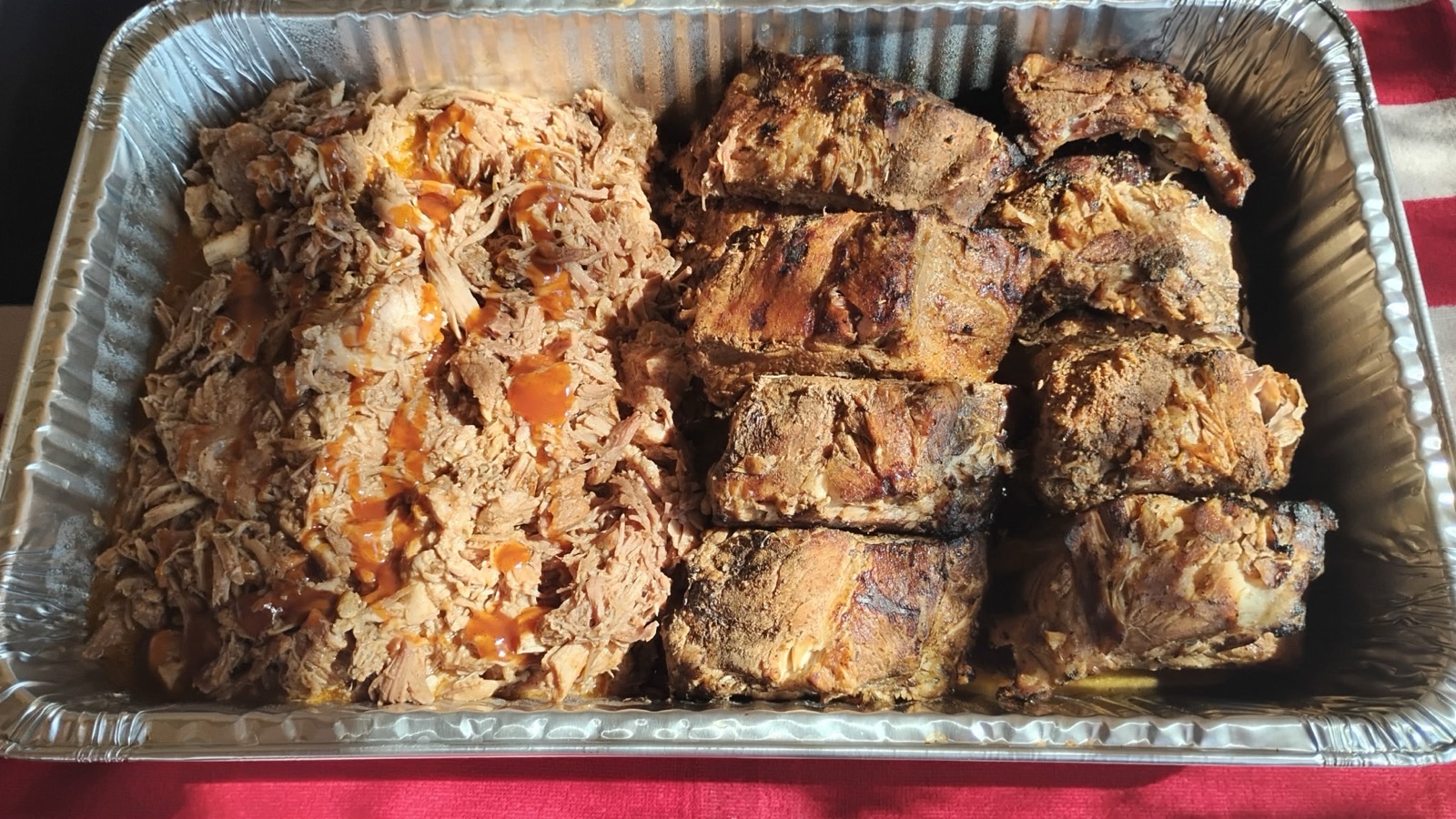 A catering pan holding pulled pork on one side and portioned slow baked baby back pork ribs on the other